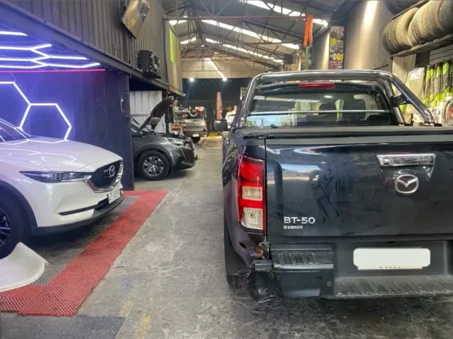 Mazda BT-50 negra con daño en la parte trasera, junto a otro auto